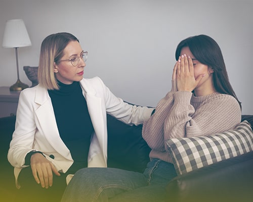 Психотерапевт сидит рядом с девушкой, которая закрывает лицо руками